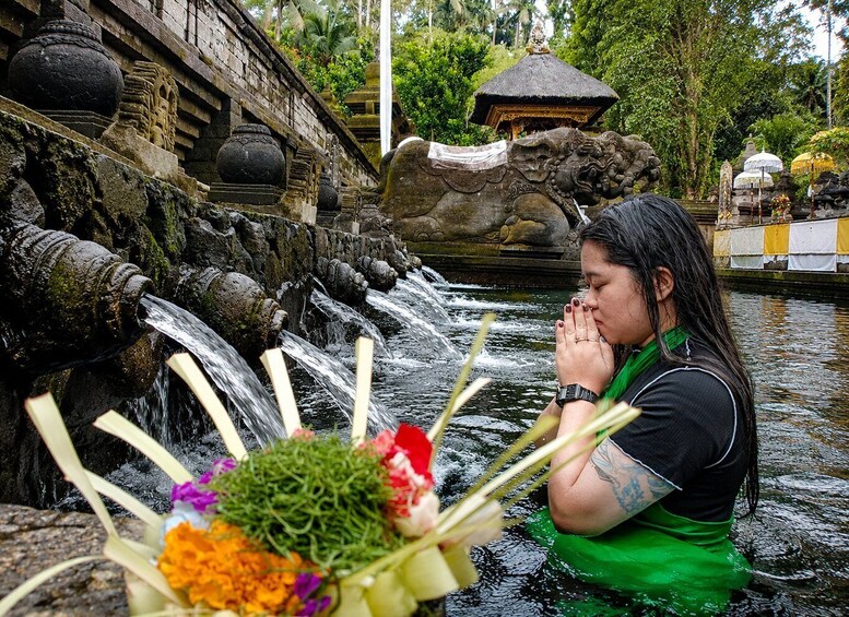 A person praying by a water feature with a temple in the background. 4