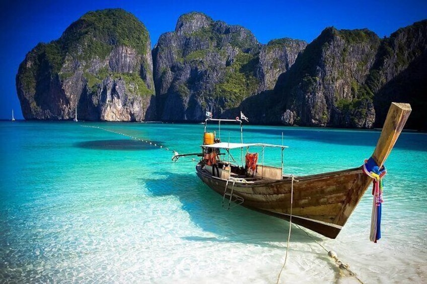 A wooden boat tied to a dock with clear turquoise water and limestone cliffs in the background. 3