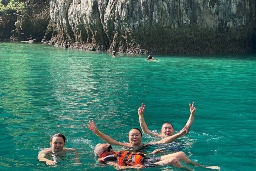 A group of people floating on a clear turquoise sea with rocky cliffs in the background. 2