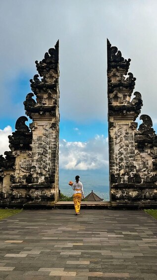 A person walking through ancient stone gates with intricate carvings, leading to a traditional Balinese temple. 3