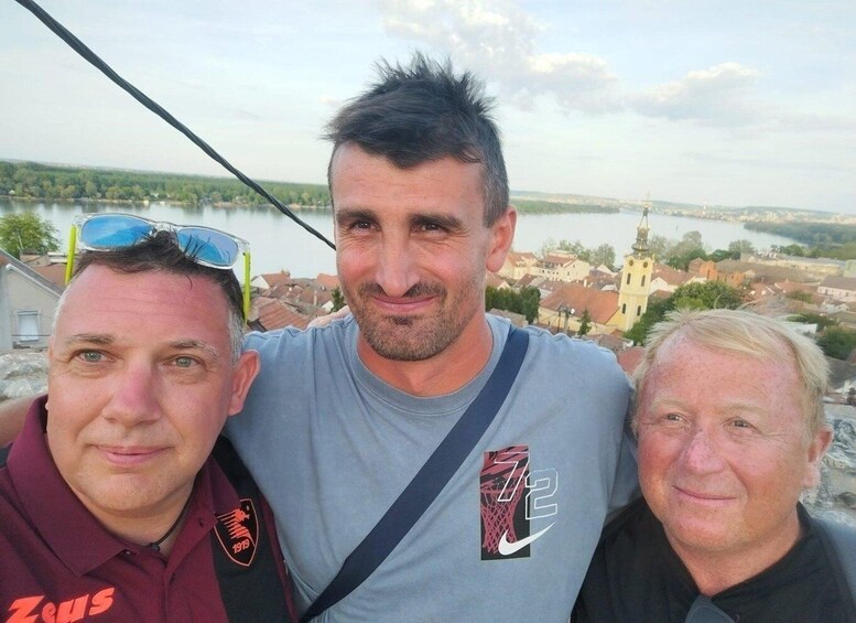 Three people standing on a bridge with a river and town in the background. 2