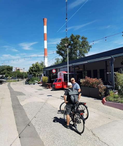 A man on a bicycle, a red truck, and a tall chimney in the background. 1