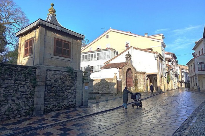 A cobblestone street with historic buildings, a stone wall, and a small tower. 2