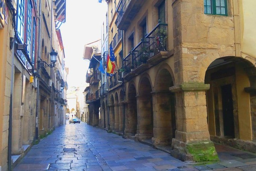 A narrow cobblestone street flanked by historic buildings with arched windows and balconies. 3