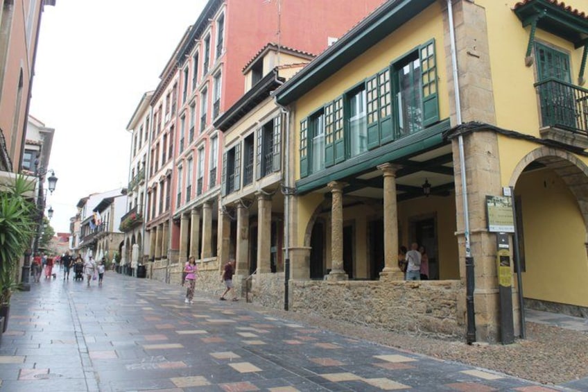 A pedestrian street with buildings, a tiled pavement, and a few people walking. 1