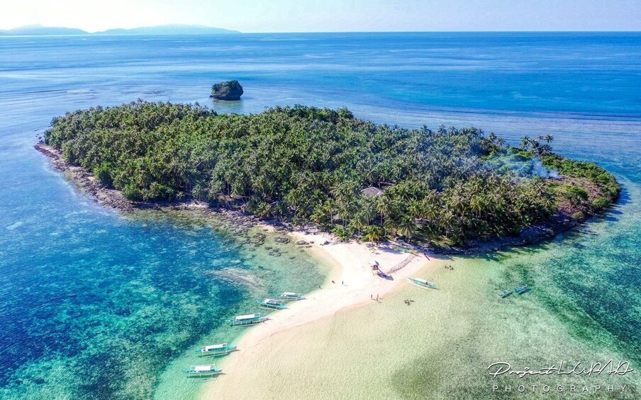 An aerial view of a tropical island with a clear beach, dense forest, and a small rocky outcrop in the water. 2