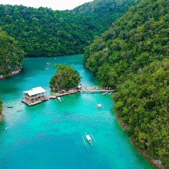 A tropical island with a wooden house and dock, surrounded by turquoise waters and dense greenery. 1