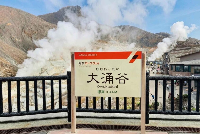 A sign indicating the Hakone Ropeway with a view of steam rising from the mountains. 3