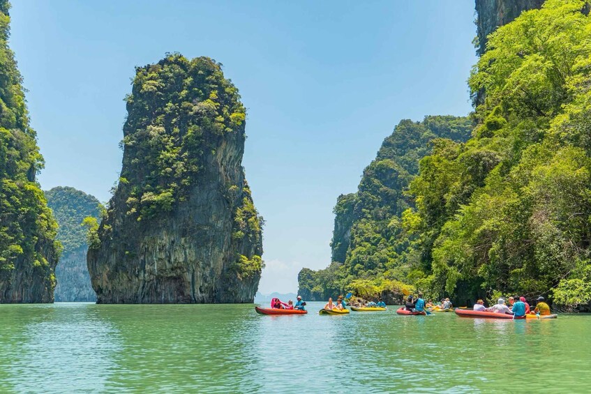 A group of people kayaking on a river surrounded by tall, green limestone cliffs. 2