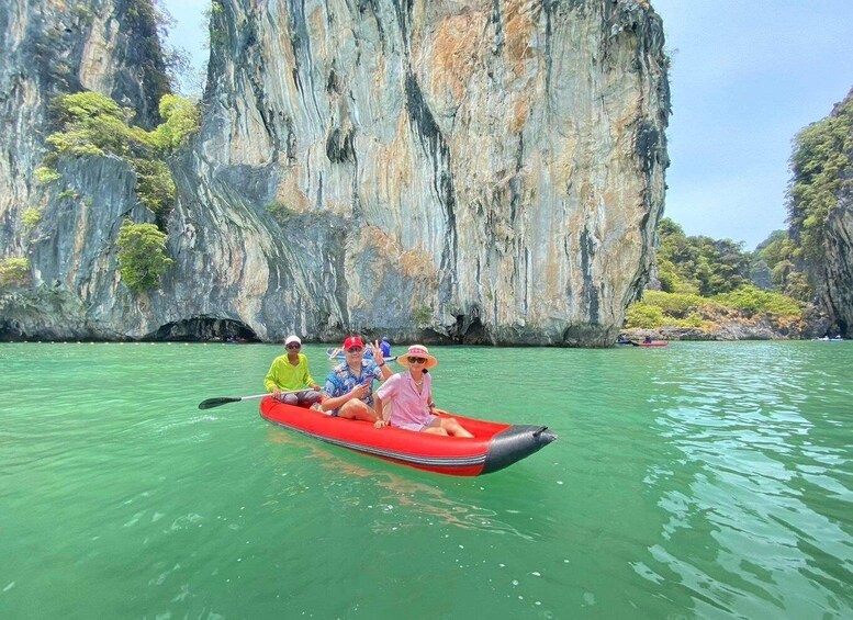A group of people in a red inflatable raft on calm green water, surrounded by large limestone cliffs. 5