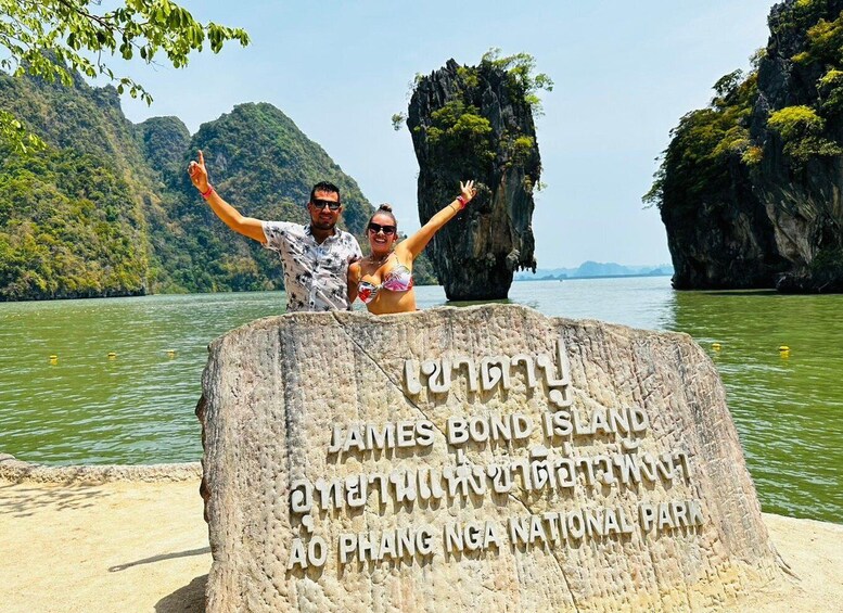 A couple standing on a stone monument with arms raised, surrounded by a water body and limestone cliffs. 2