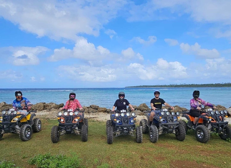 Five people on ATVs by a coastal area with clear skies. 5