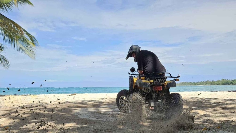 A person on a quad bike on a sandy beach with the ocean in the background. 1