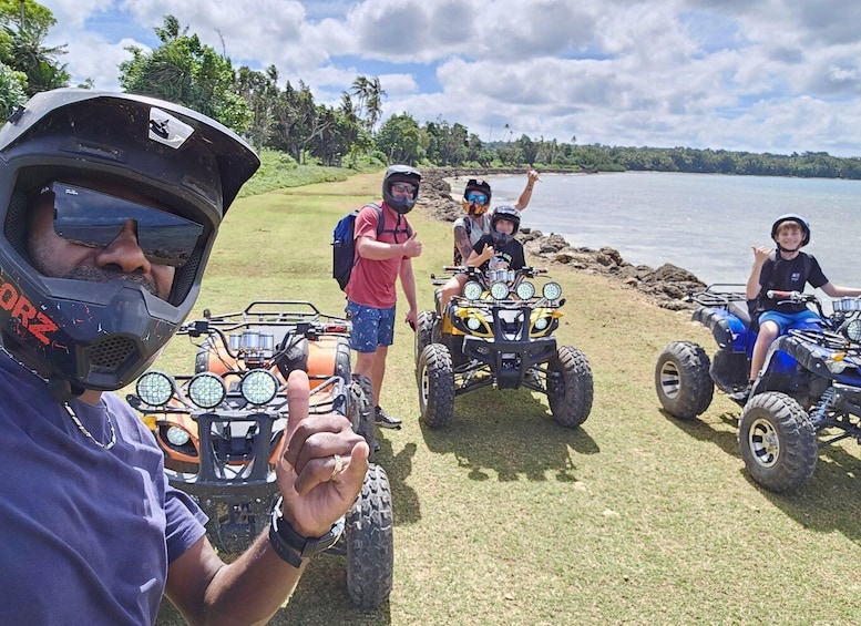 A group of people on ATVs near a body of water with a grassy area and trees in the background. 2