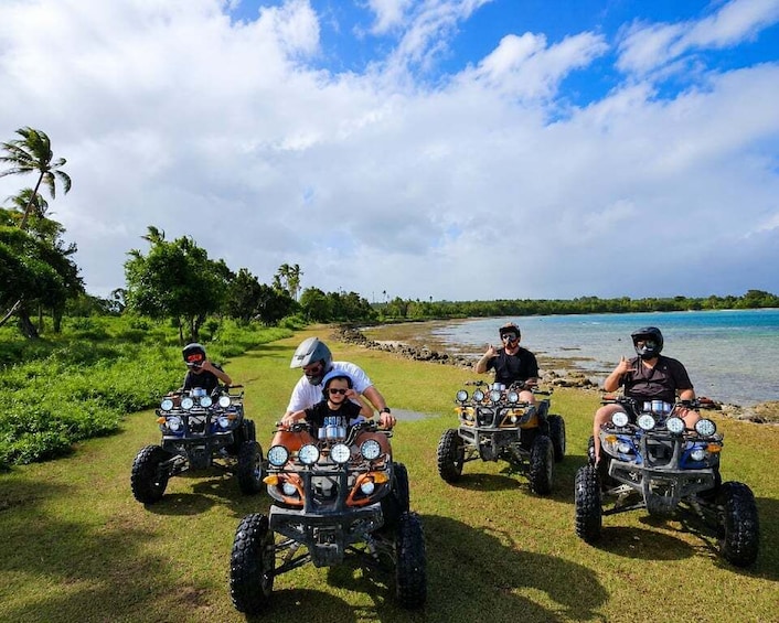 Four people on ATVs near a body of water with palm trees and a clear sky. 3