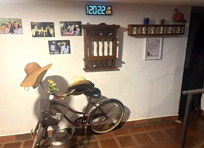 A bicycle with a basket and a sun hat, a wall clock, and several framed photos. 1