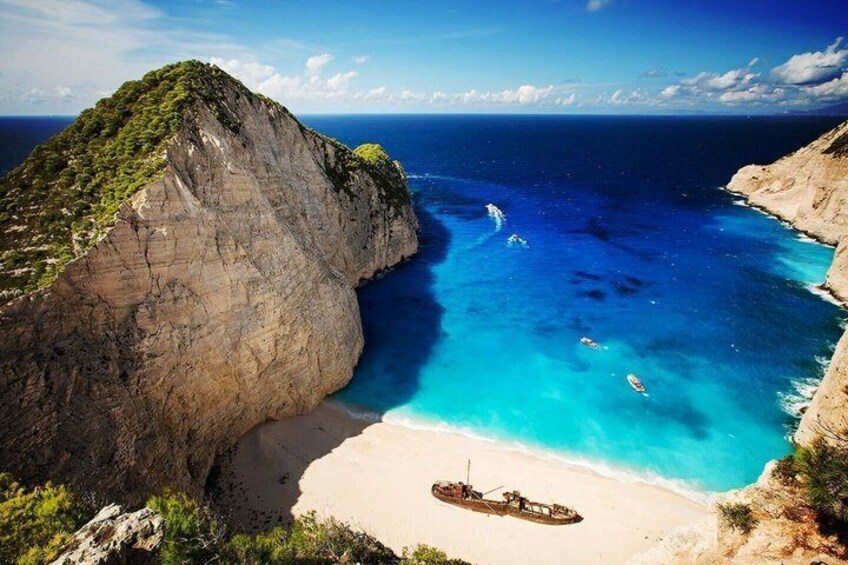 A coastal landscape with a large cliff, clear blue waters, and a boat on the beach. 1