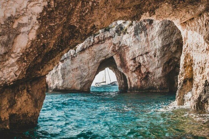 A natural rock arch over a body of water with a sailboat in the distance. 3