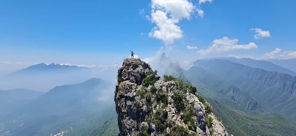 A person standing on a mountain peak with a clear sky and distant mountains. 1