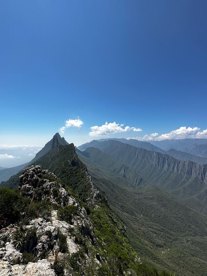A mountain landscape with a prominent peak, lush greenery, and distant mountain ranges under a clear blue sky. 4