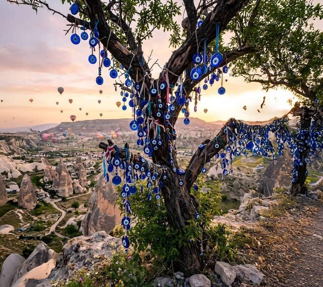 A tree adorned with blue ornaments against a backdrop of a mountainous landscape and hot air balloons. 2