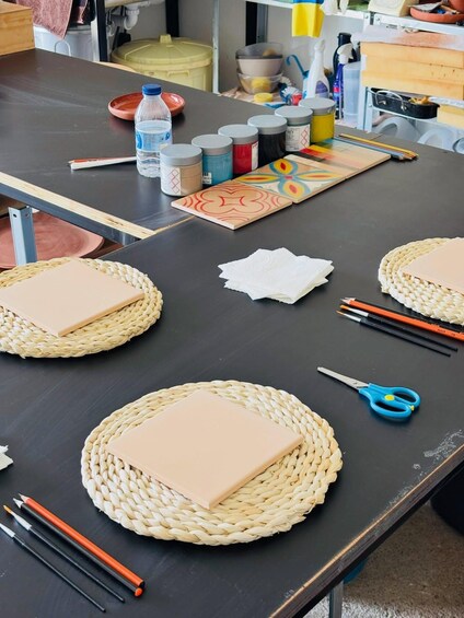 A workspace with woven mats, notebooks, paintbrushes, and art supplies. 3