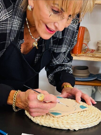 A person painting a design on a woven mat. 5
