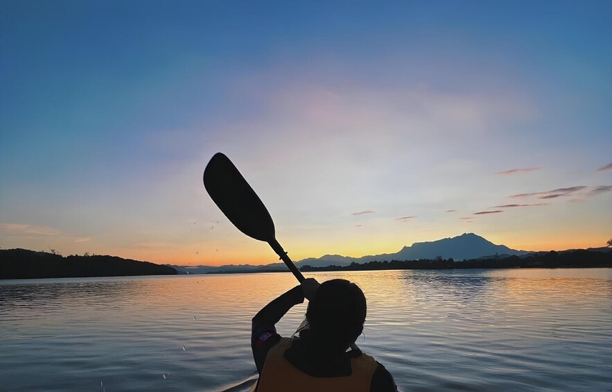 A kayaker paddling on a calm lake with mountains in the background during sunset. 1