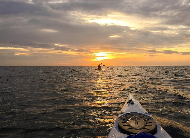 A kayaker paddling towards a sunset over the ocean. 2