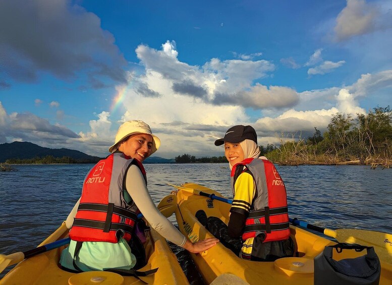 Two people in a yellow canoe on a calm river, wearing life jackets and hats, with a rainbow in the background. 5