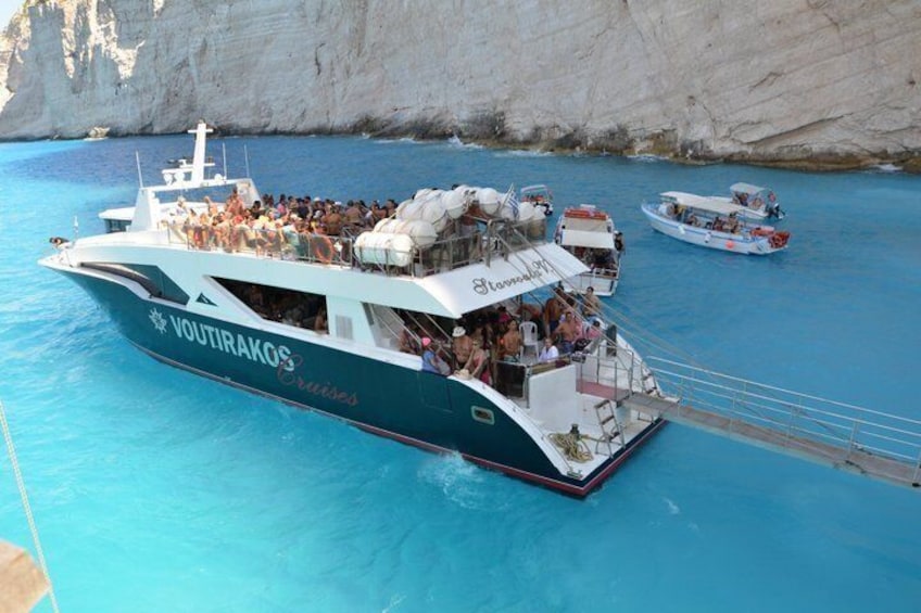 A cruise ship named 'VOUTIRAKOS Cruises' with passengers on deck, surrounded by clear blue water and white cliffs. 5