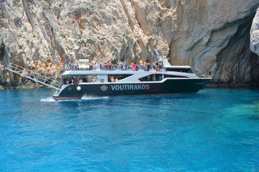 A boat named 'VOUTIRAKOS' with passengers, sailing near rocky cliffs. 2