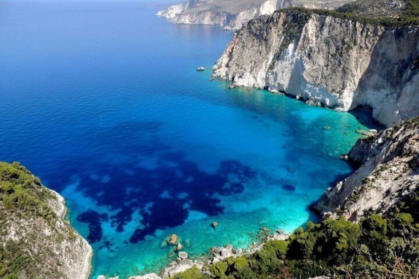 A coastal landscape with clear blue waters, rocky cliffs, and sparse vegetation. 1