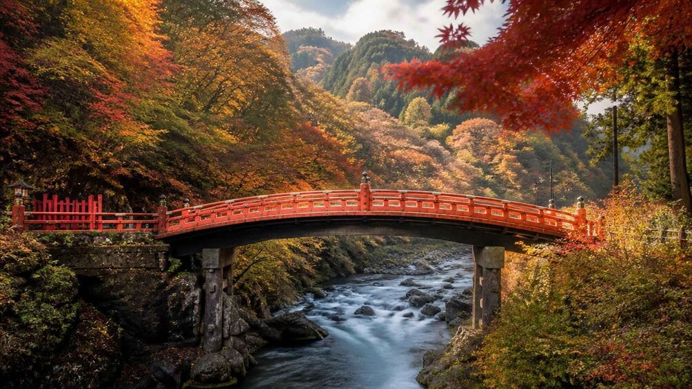 A red bridge over a flowing river, surrounded by autumn foliage. 2