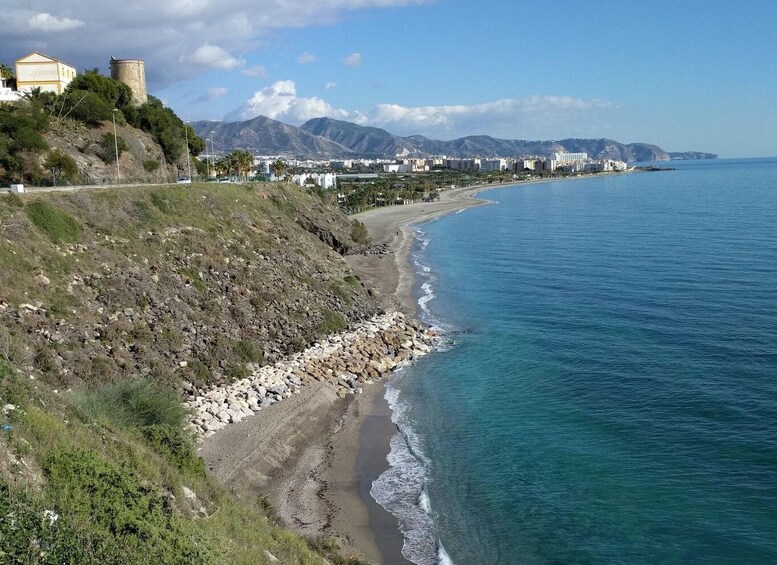A coastal landscape with a rocky beach, a clear blue sea, and a city in the background. 5