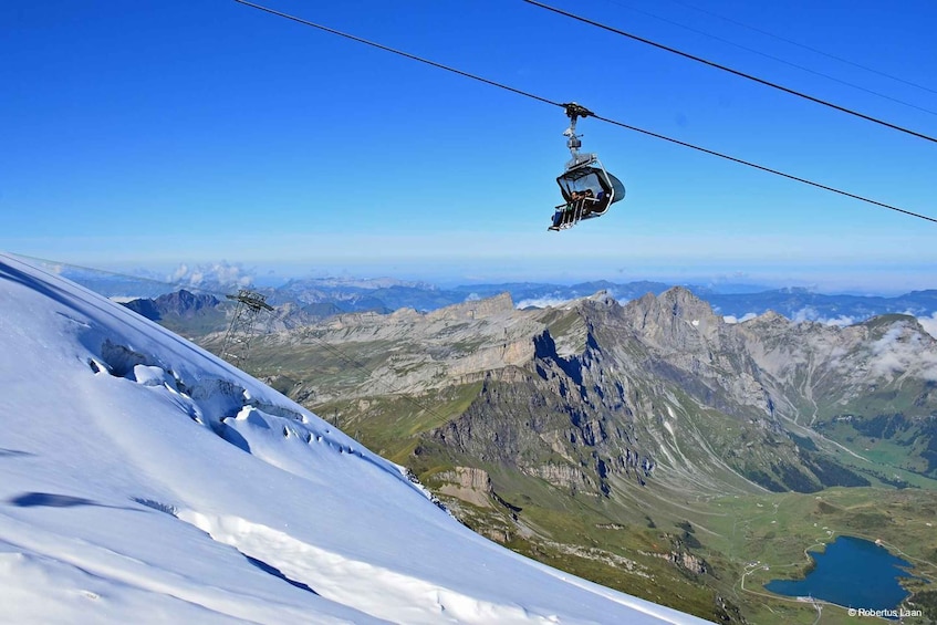 A cable car ascending a snowy mountain with a clear sky and a valley below. 1