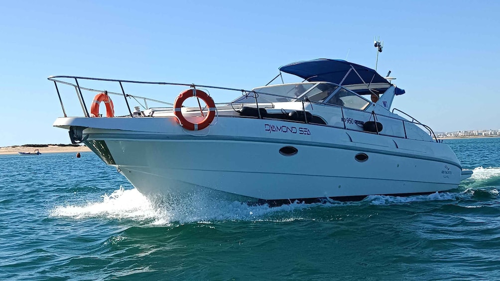 A white yacht named 'DIAMOND SEA' with two life rings and a blue canopy, cruising on clear blue waters. 1