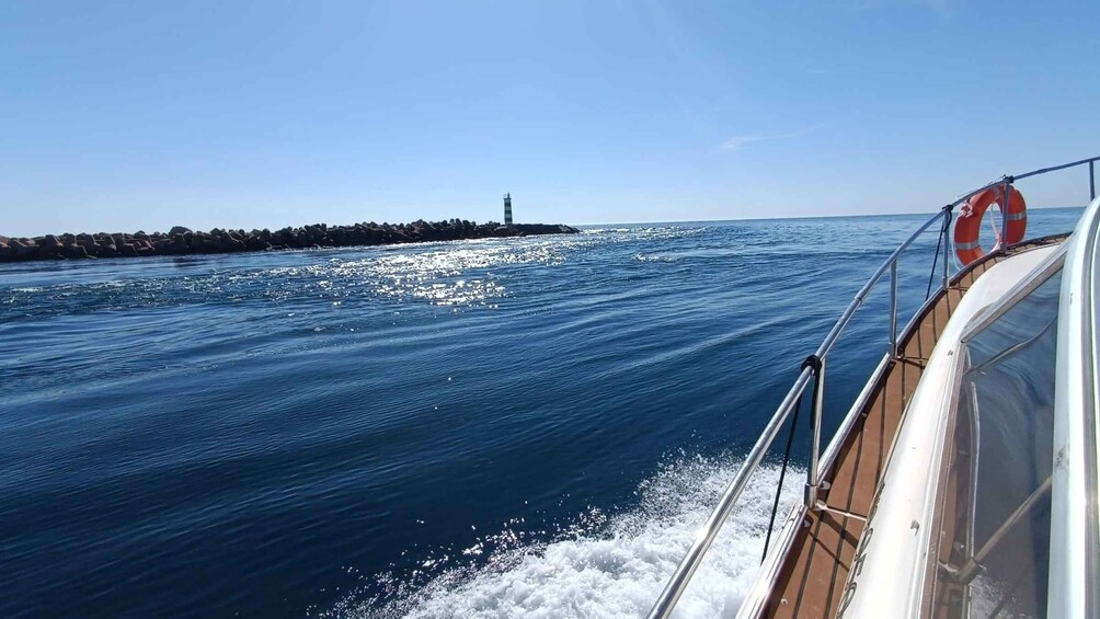 A boat on a calm sea with a rocky shoreline and a lighthouse in the distance. 5