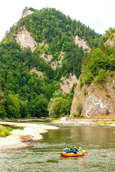 A group of people in a yellow raft on a river surrounded by dense green forest and rocky cliffs. 3