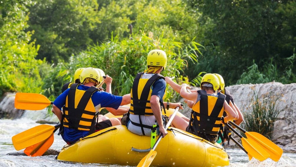 Three people in yellow helmets and life vests on a yellow raft, paddling through a river surrounded by greenery. 4
