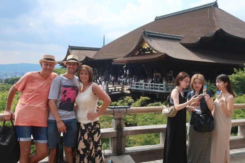A group of people standing in front of a traditional building with a curved roof, a stone railing, and a view of greenery and distant mountains. 4