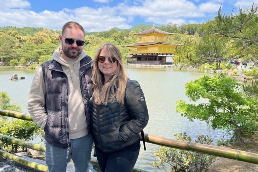 A couple standing by a calm lake with a traditional building in the background. 2