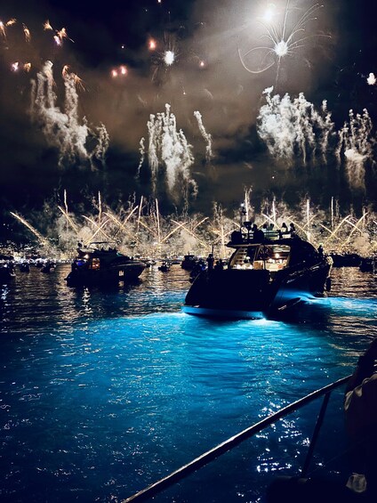 A nighttime scene with boats on water, fireworks in the sky, and a cityscape in the background. 4