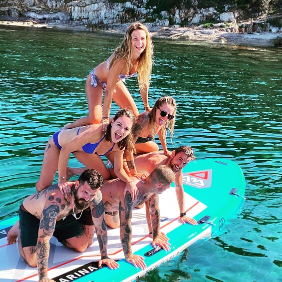 A group of people on a surfboard in a body of water with rocky cliffs in the background. 2