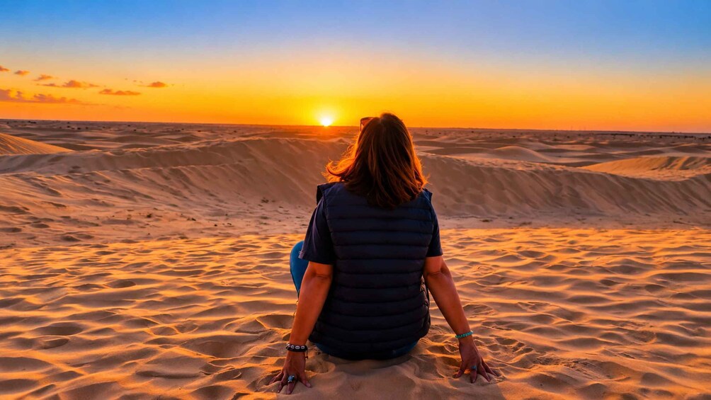 A person sitting on sand dunes facing a sunset. 1