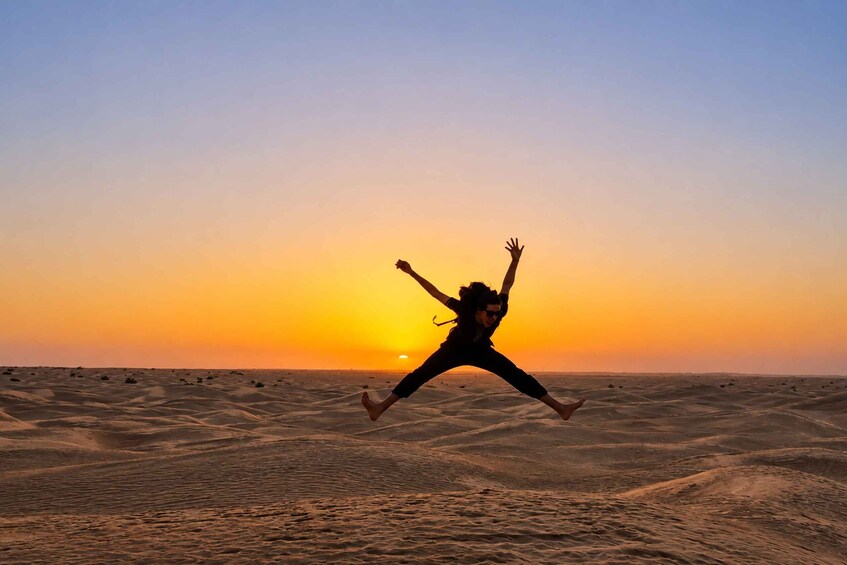 A person jumping in a desert at sunset. 5