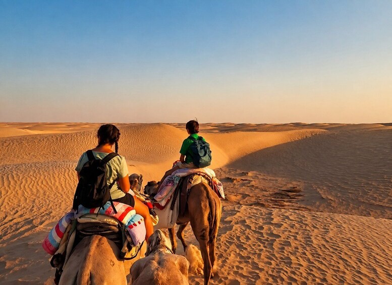 Two people riding camels through a desert landscape with sand dunes. 4