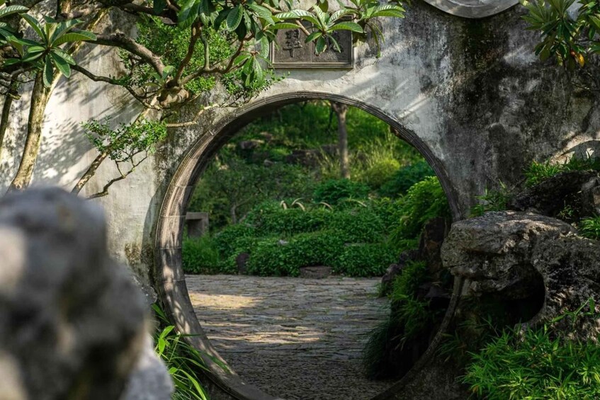 A stone archway with a circular opening, surrounded by lush greenery and a stone path. 1