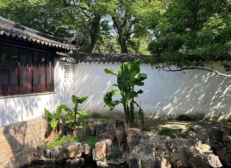 A traditional building with a tiled roof, a stone wall, and a small pond with rocks and plants. 3