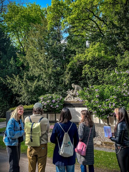 A group of people standing in a park with a statue and inscriptions in the background. 5